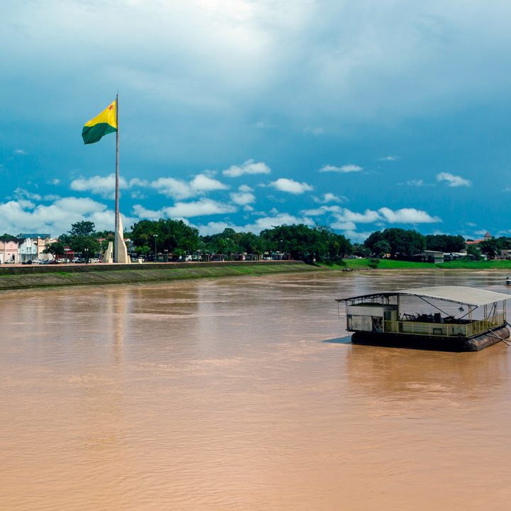 Image of the Acre state flag flying at the edge of a river